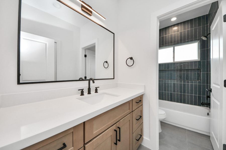 Discover the elegance of a sleek, modern third full bathroom, featuring a spacious double vanity and a chic, tiled shower/bathtub combo, perfect for both guests and family.