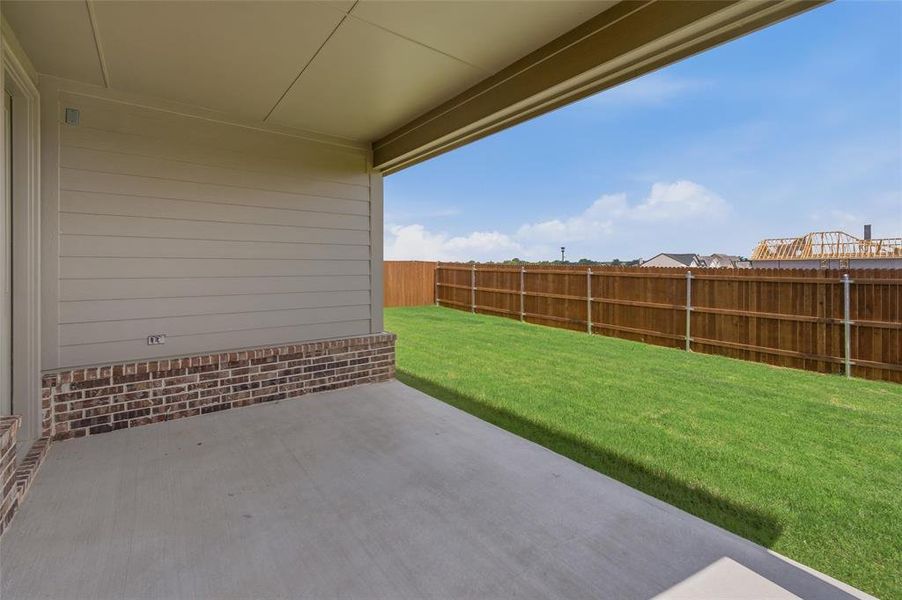 Covered concrete patio with a painted ceiling, brick and siding exterior, expansive green lawn, and a perimeter wood fence