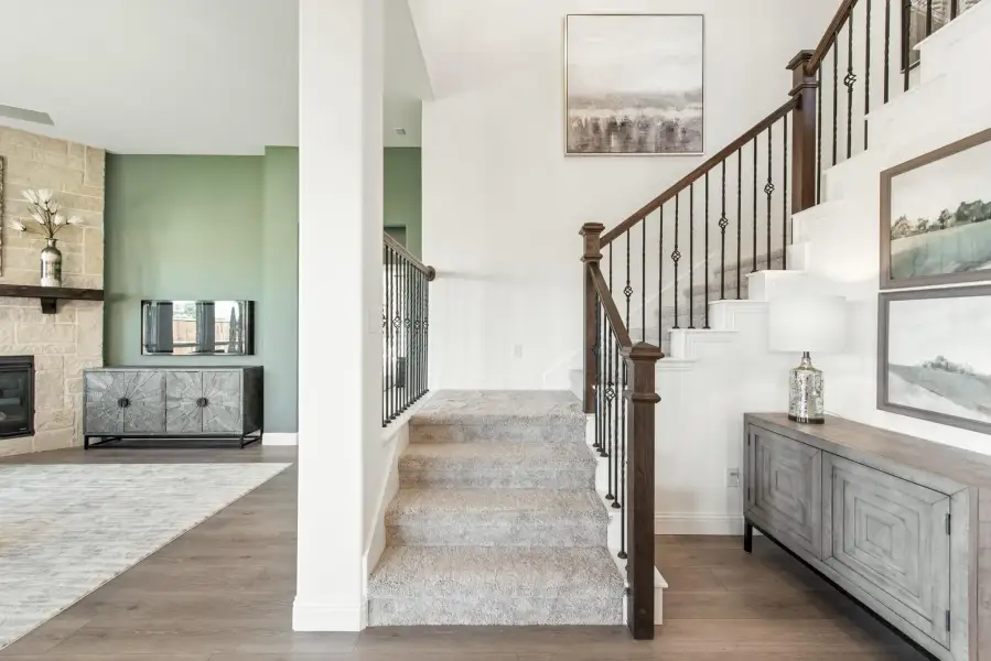 Carpeted staircase with dark wood and iron railings, open to living room with stone fireplace and hardwood floors