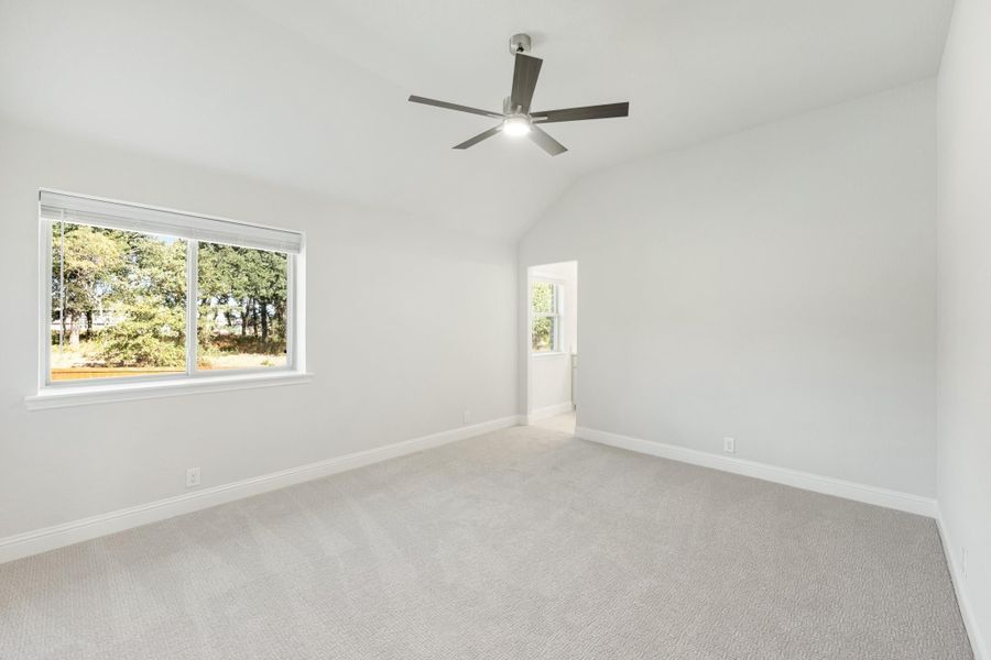 Empty bedroom with vaulted ceiling, ceiling fan, carpet flooring, and two windows