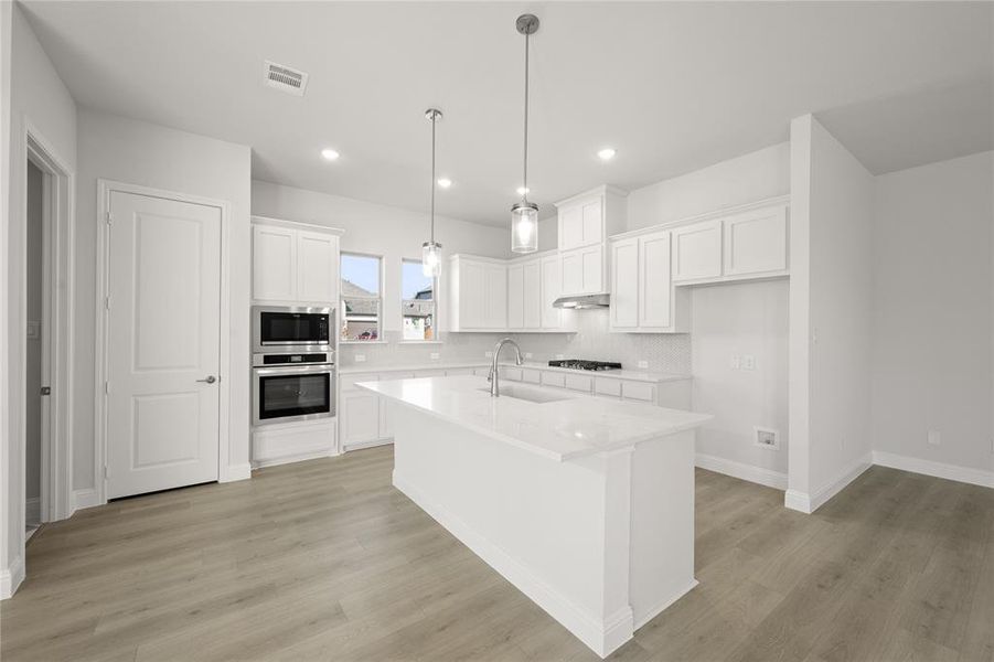 Kitchen with backsplash, a kitchen island with sink, light wood-type flooring, appliances with stainless steel finishes, and white cabinetry