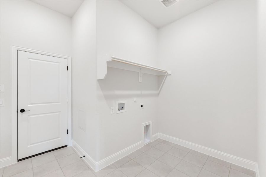 Empty laundry room with white walls, built-in shelf, washer and dryer hookups, and tile flooring Empty laundry room with white walls, built-in shelf, washer and dryer hookups, and tile flooring