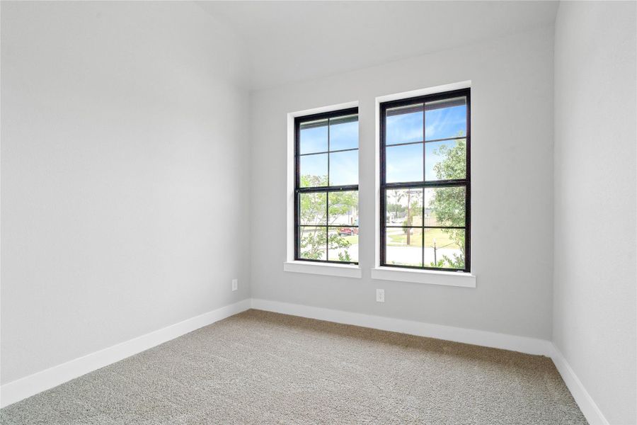 Tucked peacefully in the front of the home is this secondary bedroom. It features plush carpet flooring, neutral toned walls, and large windows.
