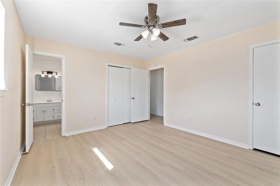 Unfurnished bedroom with light wood-style floors, ensuite bathroom, and a ceiling fan
