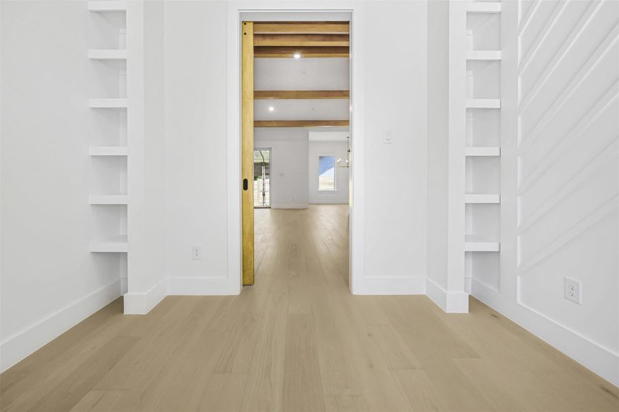 Corridor with light wood-type flooring, beamed ceiling, and built in shelves
