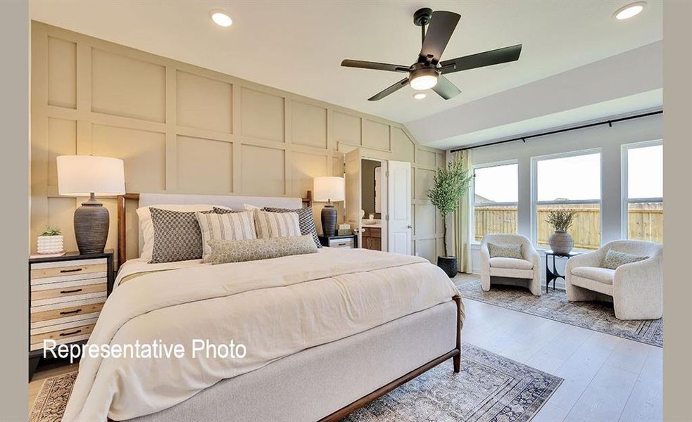 Vaulted ceiling bedroom featuring a board and batten accent wall, wood-finish flooring, a ceiling fan with integrated lighting, and multiple windows