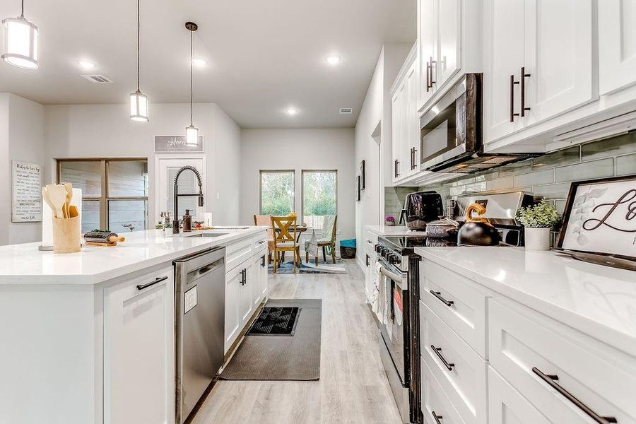 Kitchen with pendant lighting, light wood-type flooring, an island with sink, appliances with stainless steel finishes, and white cabinetry