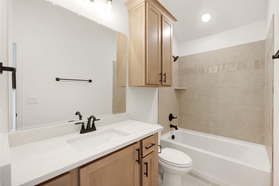 Bathroom with single vanity, wood cabinets, white countertop, and tiled tub-shower combo with dark hardware