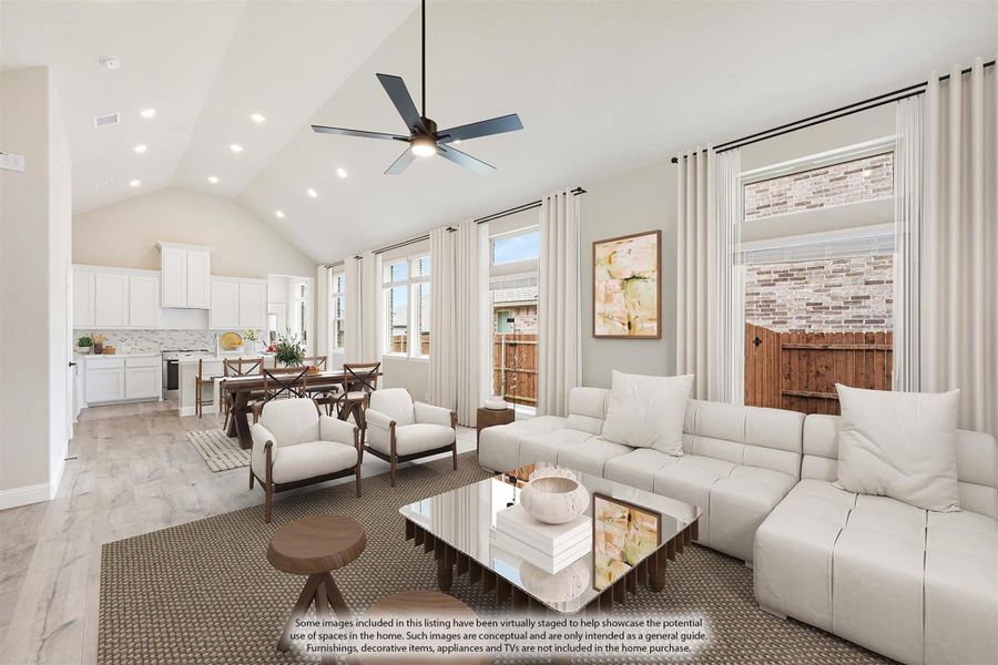 Open-concept living room with vaulted ceiling, ceiling fan, white sofa, and kitchen visible in background
