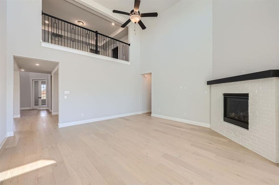 Unfurnished living room with light hardwood / wood-style flooring, a fireplace, ceiling fan, and high vaulted ceiling