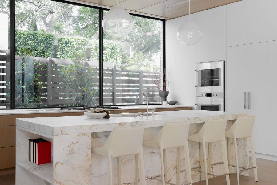 Kitchen with modern cabinets, light stone countertops, white cabinets, hanging light fixtures, and a kitchen island with sink