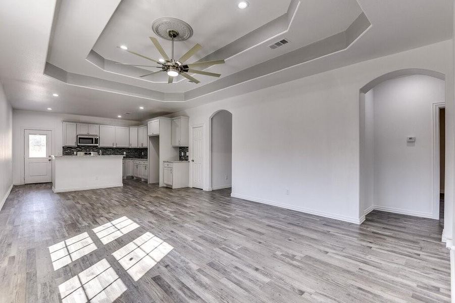 Unfurnished living room with ceiling fan, a tray ceiling, and light wood-type flooring