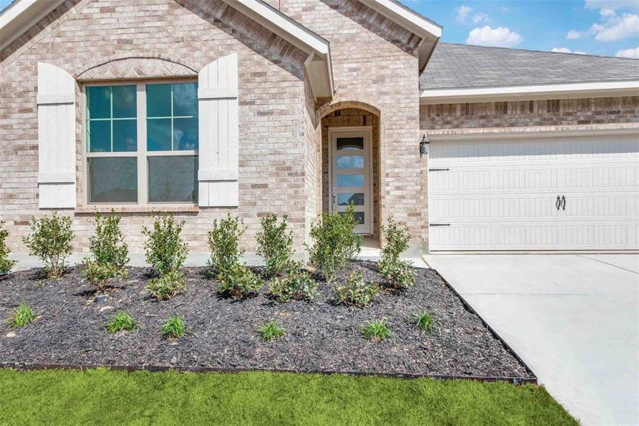 View of exterior entry with a garage, brick siding, and driveway
