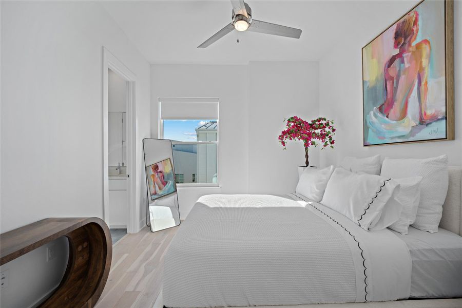 Bright bedroom featuring light wood-finish flooring, a contemporary ceiling fan, and a window with roller shade