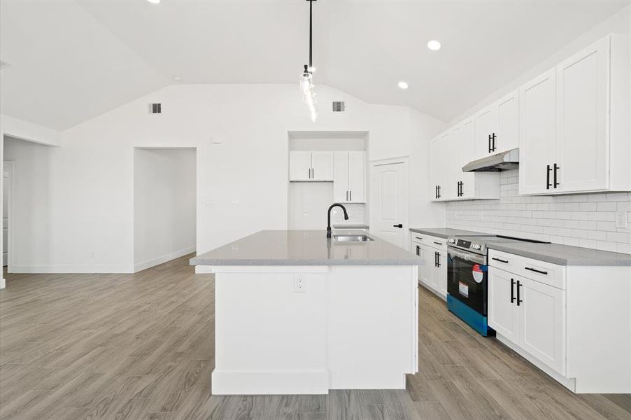 This is a spacious, modern kitchen with white cabinetry, stainless steel appliances, a large center island, and sleek gray flooring. The open floor plan allows for a seamless transition to the living area.