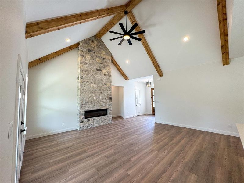 Unfurnished living room with beam ceiling, high vaulted ceiling, a fireplace, wood finished floors, and baseboards Unfurnished living room with beam ceiling, high vaulted ceiling, a fireplace, wood finished floors, and baseboards