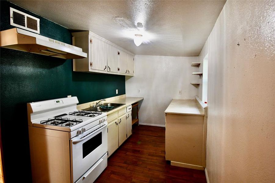Kitchen featuring white gas stove, light countertops, under cabinet range hood, a textured wall, and open shelves Kitchen featuring white gas stove, light countertops, under cabinet range hood, a textured wall, and open shelves