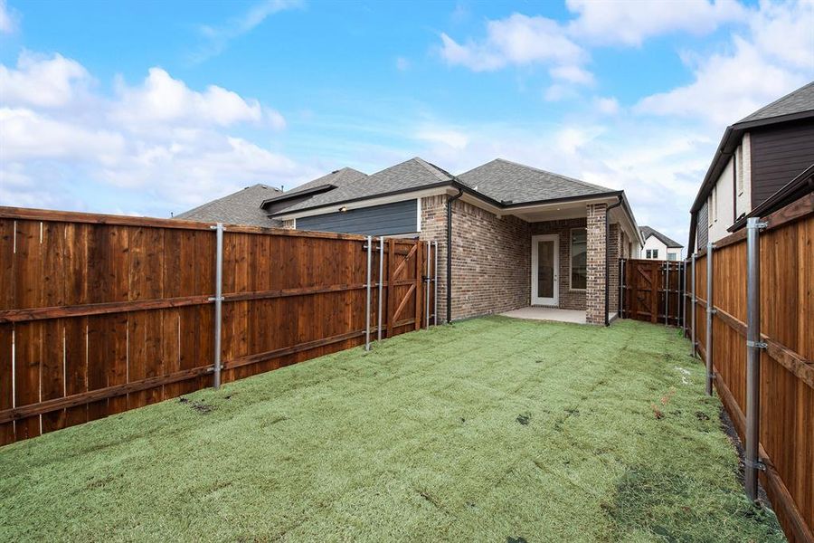 Rear view of property with a shingled roof, a patio, brick siding, a gate, and a fenced backyard Rear view of property with a shingled roof, a patio, brick siding, a gate, and a fenced backyard