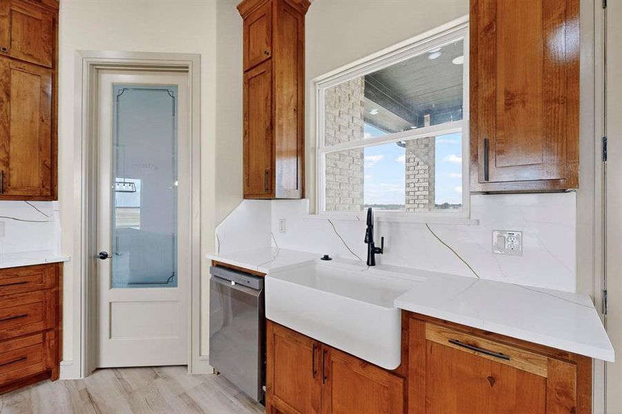 Kitchen featuring brown cabinets, dishwasher, light stone countertops, light wood-style flooring, and backsplash Kitchen featuring brown cabinets, dishwasher, light stone countertops, light wood-style flooring, and backsplash