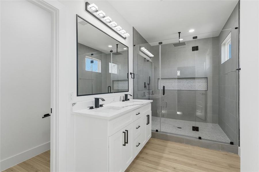 Full bath featuring double vanity, a shower stall, light wood-style floors, plenty of natural light, and recessed lighting Full bath featuring double vanity, a shower stall, light wood-style floors, plenty of natural light, and recessed lighting