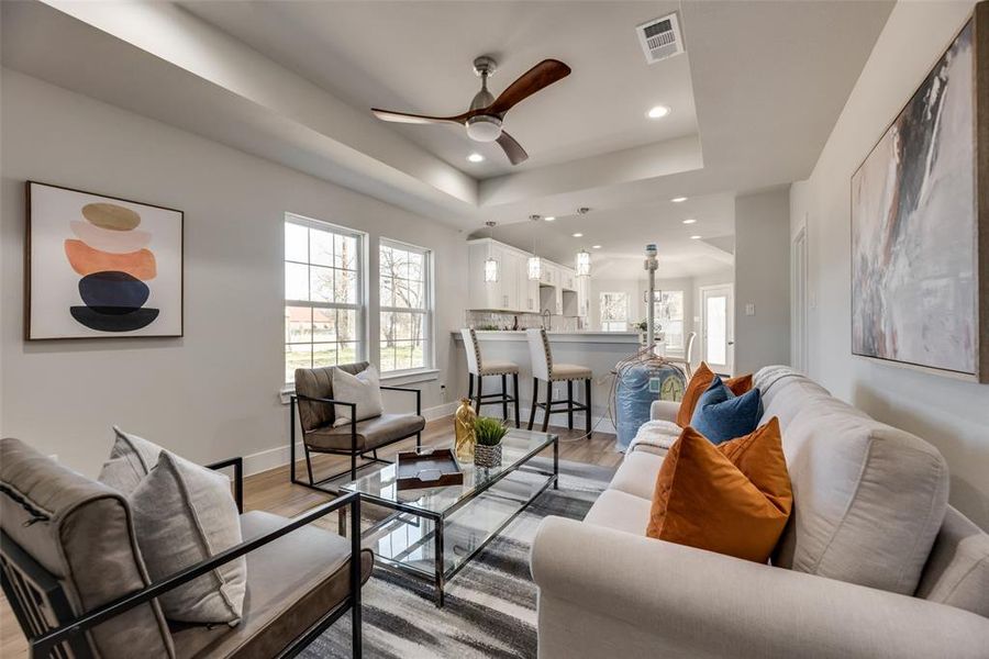 Living room with ceiling fan, light wood-type flooring, and a tray ceiling