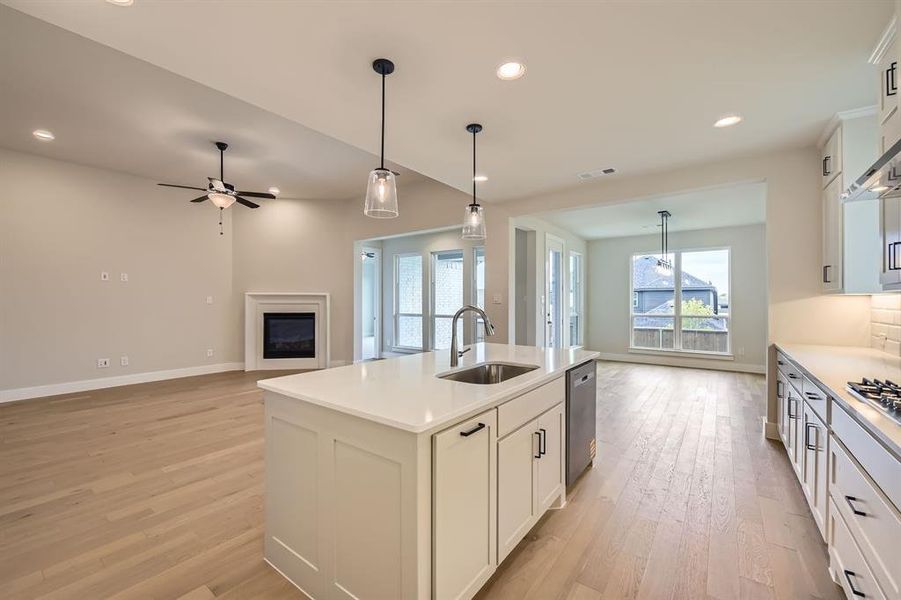 Kitchen featuring open floor plan, dishwasher, light wood-style floors, a glass covered fireplace, and ceiling fan