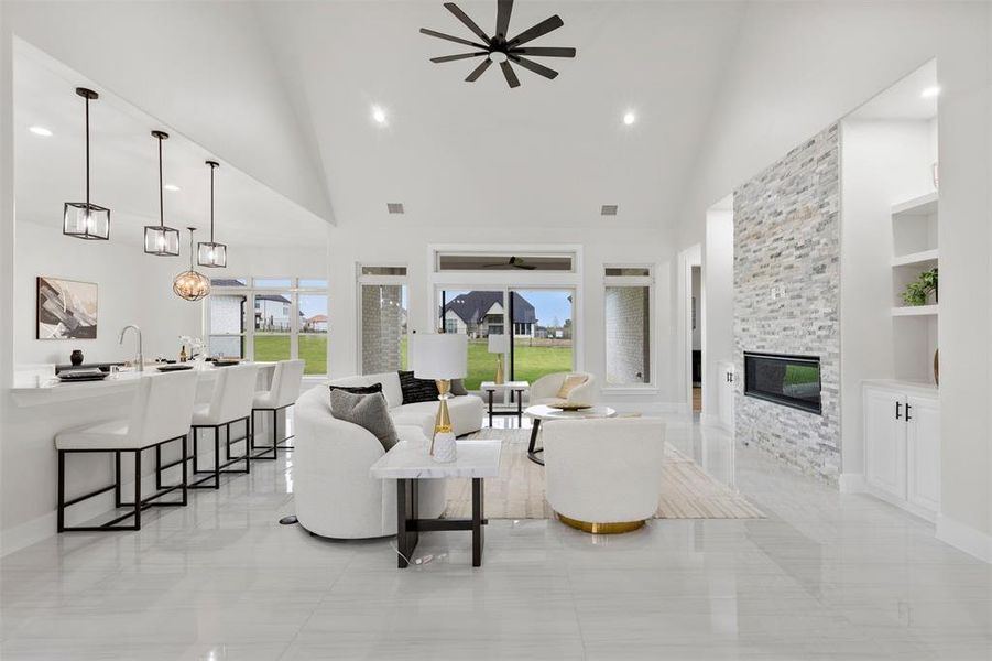 Living room with a stone fireplace, high vaulted ceiling, ceiling fan, and built in shelves.