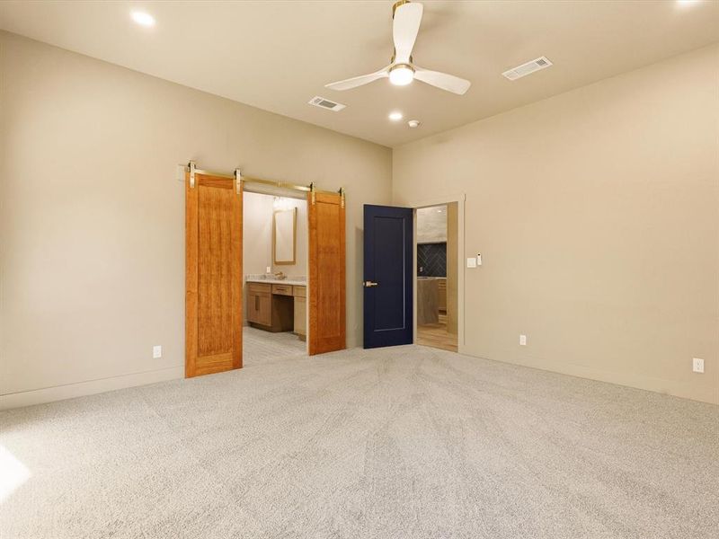 Unfurnished bedroom featuring ensuite bathroom, light colored carpet, ceiling fan, recessed lighting, and a barn door