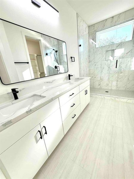 Full bath with double vanity and a marble finish shower