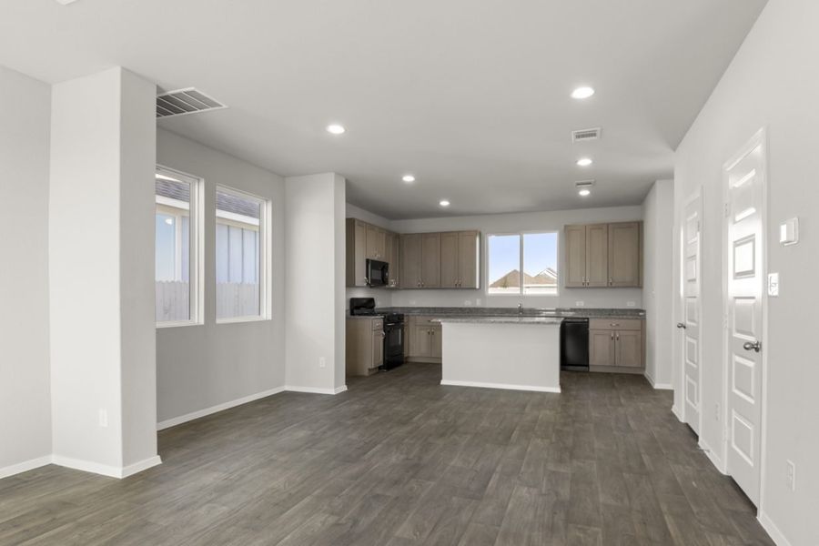 Image of a dining room with light grey walls, dark brown vinyl flooring, a dining room area, and a kitchen in the distance