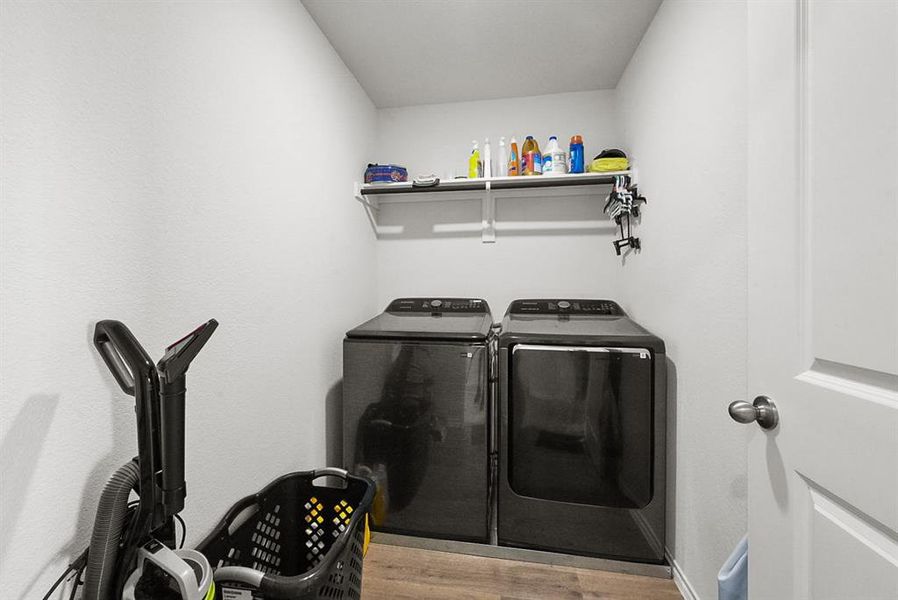 Dedicated utility space featuring wood-finish flooring, a white wall-mounted shelf, and a white paneled door with a brushed nickel knob