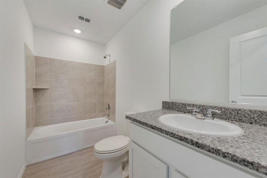 Full bathroom with tiled shower / bath, vanity, hardwood / wood-style floors, and toilet