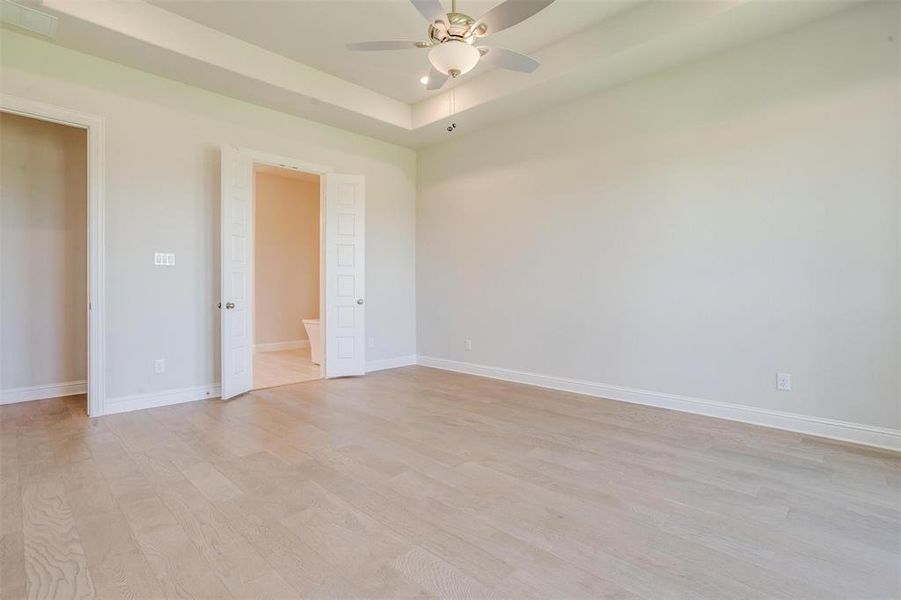 Unfurnished bedroom with ceiling fan, connected bathroom, light hardwood / wood-style flooring, and a tray ceiling