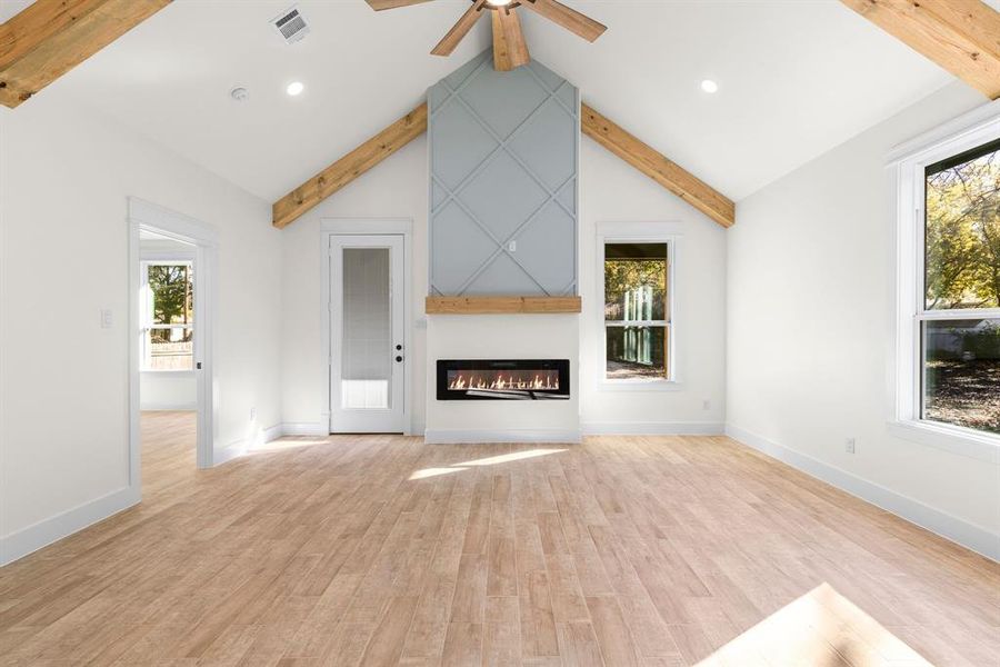 Unfurnished living room featuring a large fireplace, a healthy amount of sunlight, light wood-type flooring, and beam ceiling