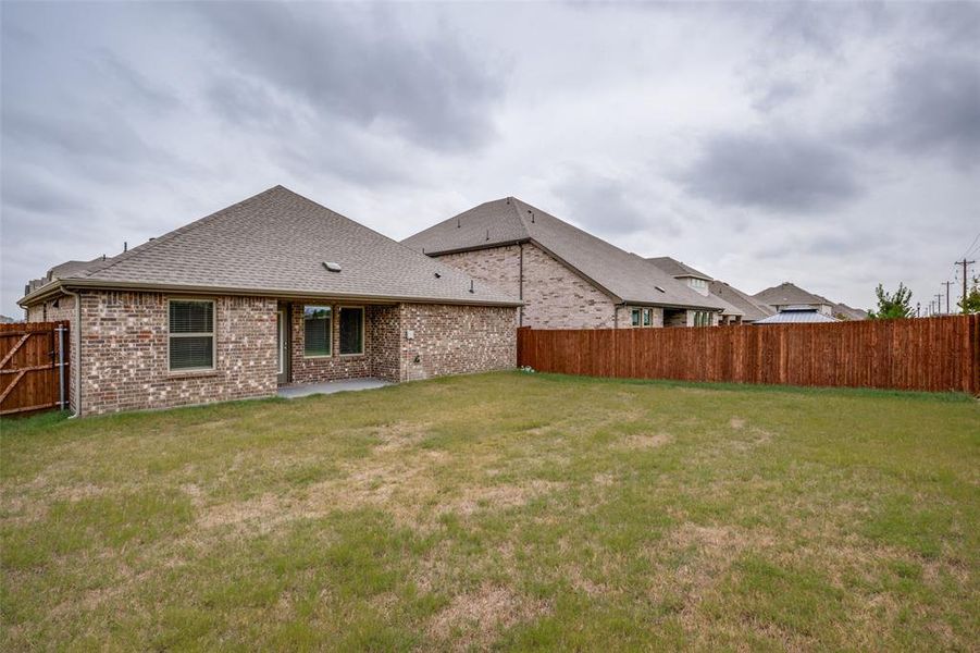 Rear view of property with a shingled roof, a fenced backyard, brick siding, and a patio area