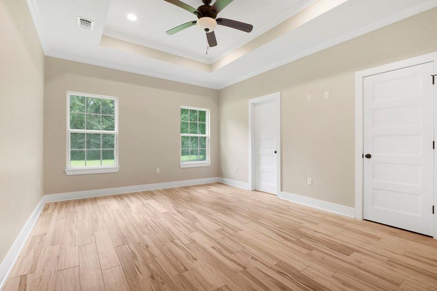 This room features light wood flooring, neutral walls, and a tray ceiling with recessed lighting and a ceiling fan. It has two large windows offering natural light and two white doors for access. This room features light wood flooring, neutral walls, and a tray ceiling with recessed lighting and a ceiling fan. It has two large windows offering natural light and two white doors for access.