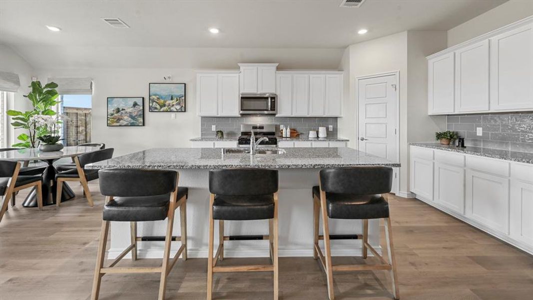 Kitchen featuring white cabinets, light stone countertops, a center island with sink, backsplash, and recessed lighting