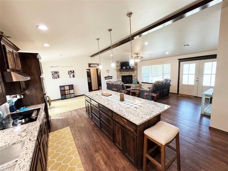 Kitchen featuring dark brown cabinets, light stone counters, a breakfast bar, open floor plan, and decorative light fixtures Kitchen featuring dark brown cabinets, light stone counters, a breakfast bar, open floor plan, and decorative light fixtures