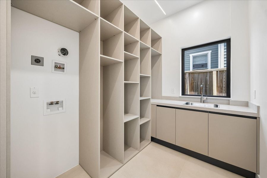 Modern utility room featuring ample storage with open shelving, a sleek countertop with an integrated sink, and a large window for natural light. Modern utility room featuring ample storage with open shelving, a sleek countertop with an integrated sink, and a large window for natural light.