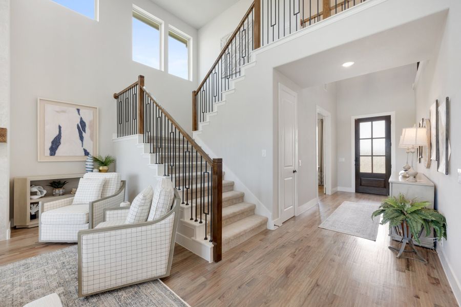 Two-story foyer with wood and iron staircase, hardwood floors, and glass front door