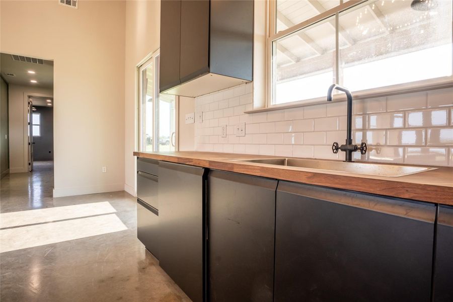 Kitchen featuring butcher block counters, decorative backsplash, finished concrete floors, and gray cabinets