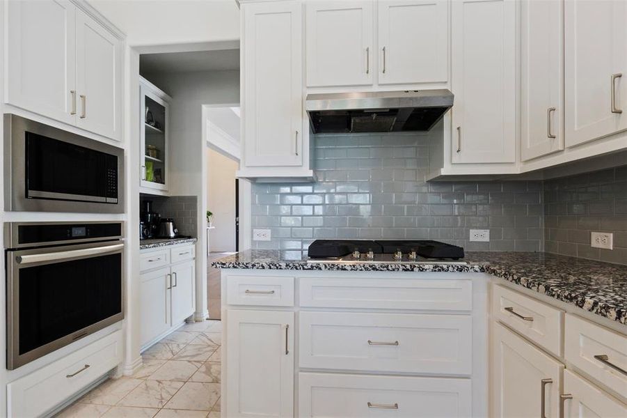 Kitchen with appliances with stainless steel finishes, tasteful backsplash, white cabinets, dark stone countertops, and light marble finish flooring