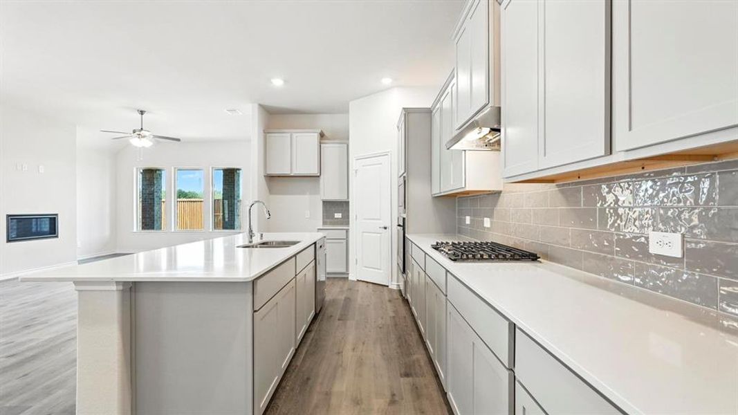 Kitchen with tasteful backsplash, gray cabinets, dark wood-style floors, ceiling fan, and an island with sink