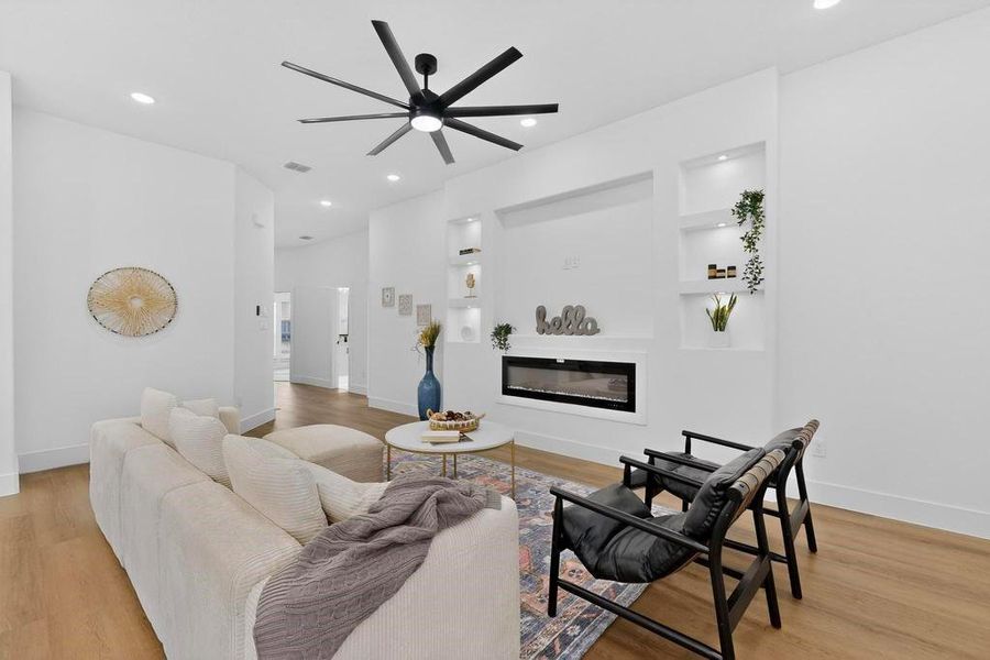 Living area featuring light wood-style floors, a glass covered fireplace, built in features, ceiling fan, and recessed lighting Living area featuring light wood-style floors, a glass covered fireplace, built in features, ceiling fan, and recessed lighting
