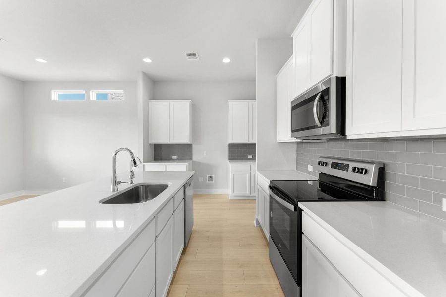 A well-lit kitchen presents a large island with sink, complemented by sleek countertops and modern appliances. A well-lit kitchen presents a large island with sink, complemented by sleek countertops and modern appliances.