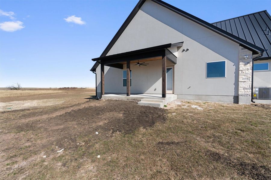 Back of property featuring a ceiling fan, a metal roof, stucco siding, a lawn, and a patio area