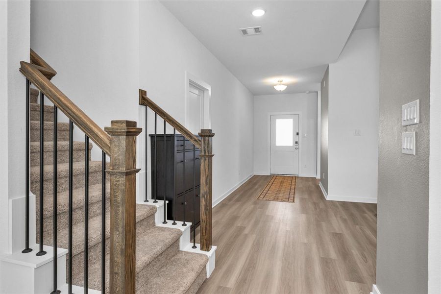 This bright and welcoming entryway features a stylish staircase with custom railing, and an open, airy layout that creates a warm first impression.