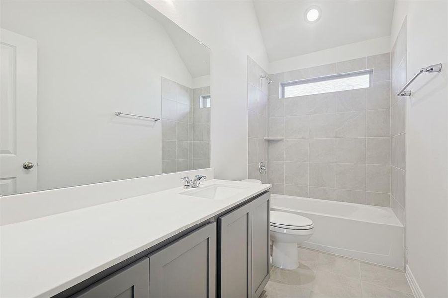 Full bathroom with tiled shower / bath combo, tile patterned floors, lofted ceiling, toilet, and vanity