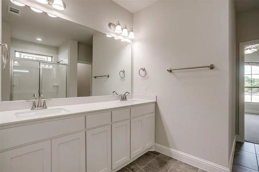 Bathroom with a shower stall, double vanity, and dark tile patterned flooring
