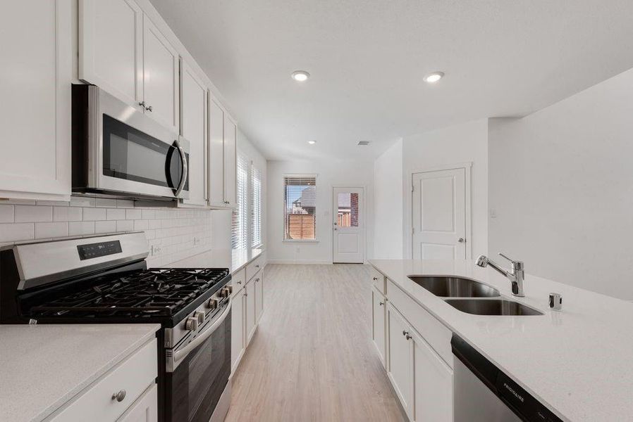 Kitchen featuring appliances with stainless steel finishes, light wood-style flooring, white cabinets, light countertops, and tasteful backsplash Kitchen featuring appliances with stainless steel finishes, light wood-style flooring, white cabinets, light countertops, and tasteful backsplash